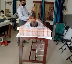 A masked therapist working with a patient lying on a couch in the treatment area