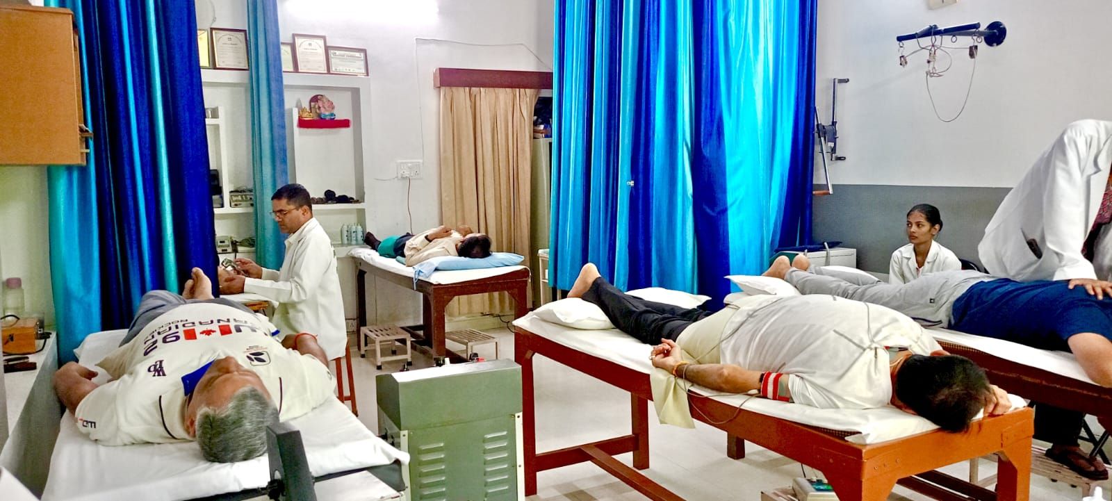 The treatment room, with patients resting on wooden couches, staff in white coats attending to them and blue curtains behind